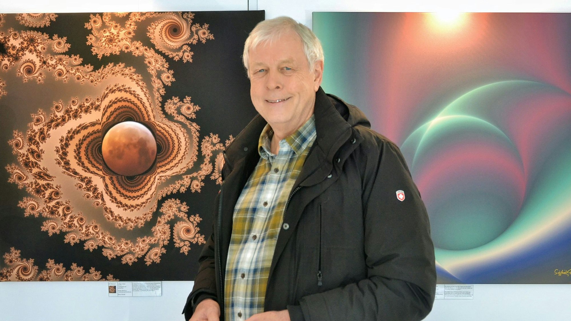 Der Künstler Siegfried Genreiths steht vor zwei seiner digitalen Bilder.
