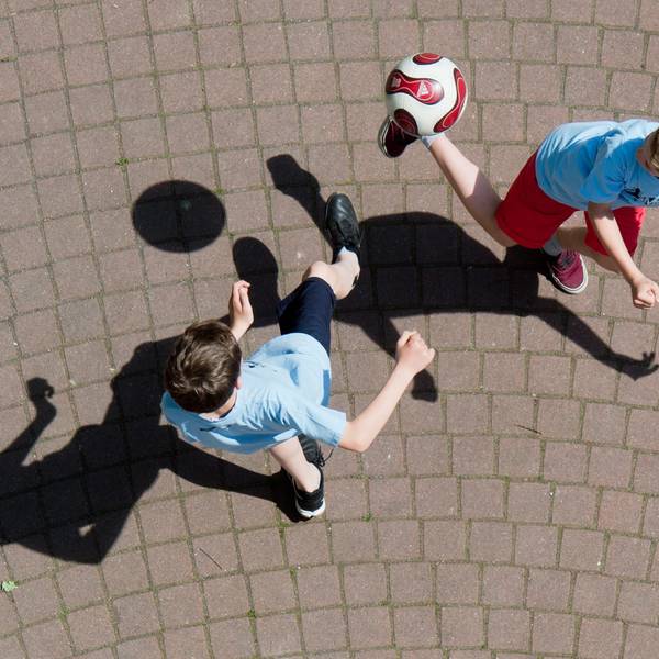 Kinder spielen Fußball auf einem Schulhof.