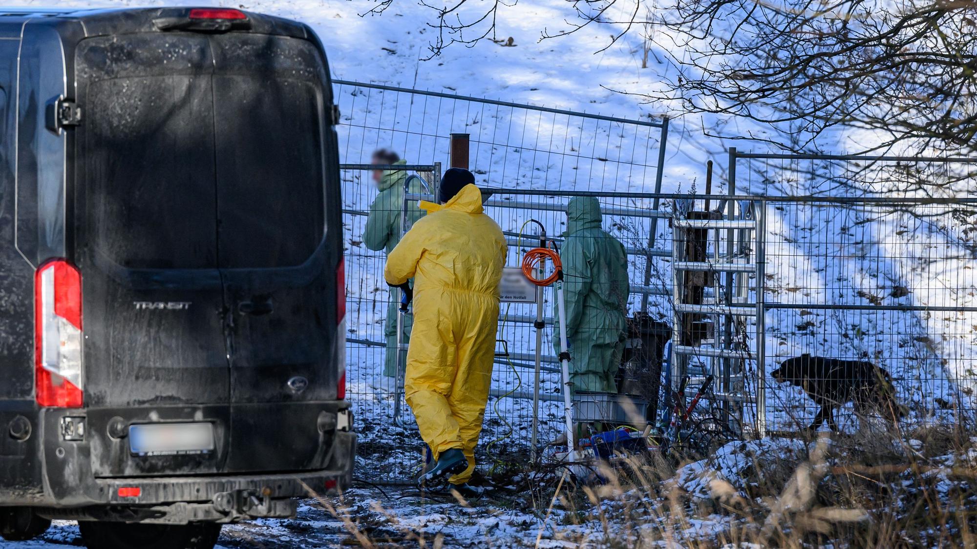 Personen in Schutzkleidung gehen über eine Weide, während Feuerwehr und Polizei das Gelände weiträumig abgesperrt haben.