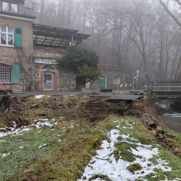Eine alte, nicht mehr benutzbare Brücke über einen Bach neben einem Gebäude.