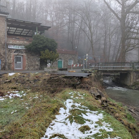 Eine alte, nicht mehr benutzbare Brücke über einen Bach neben einem Gebäude.