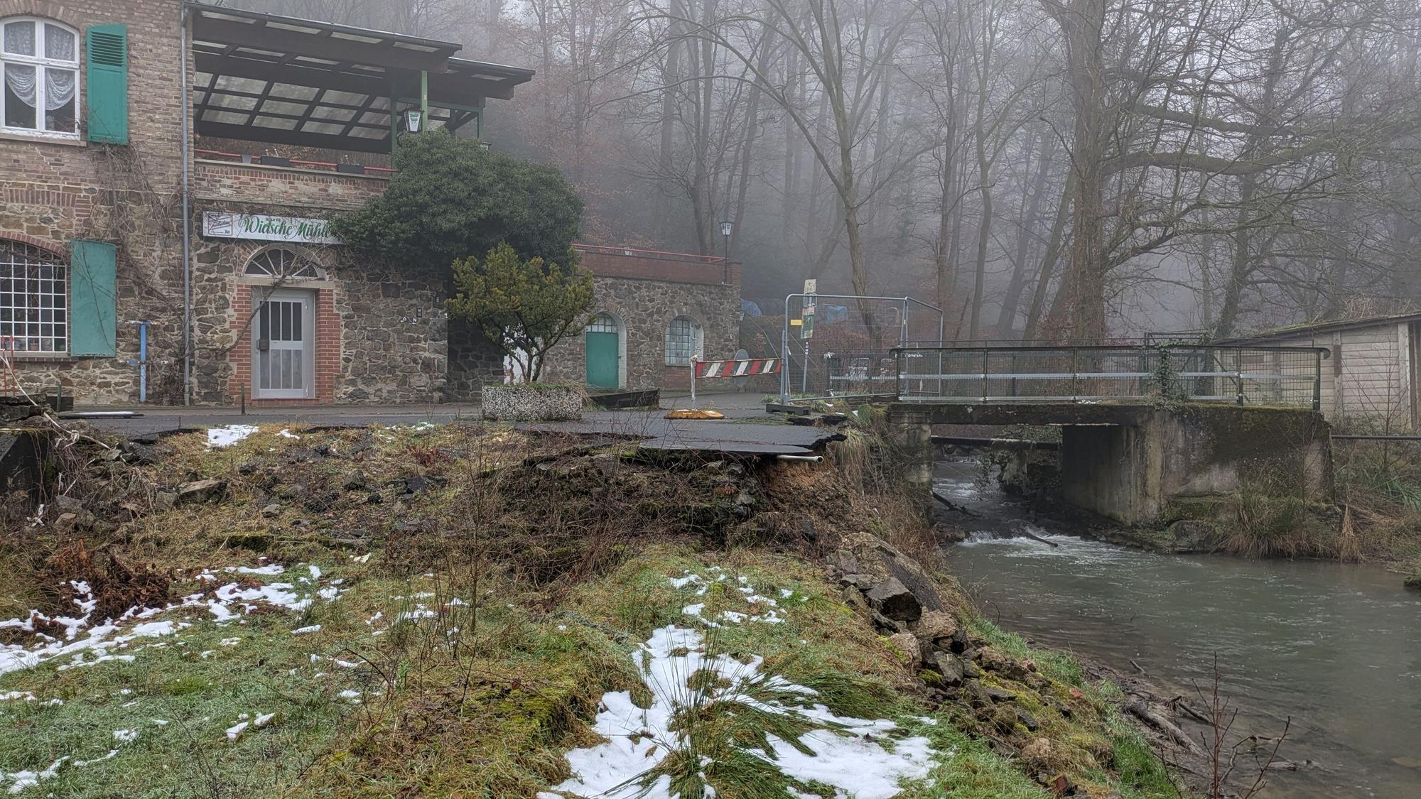 Eine alte, nicht mehr benutzbare Brücke über einen Bach neben einem Gebäude.