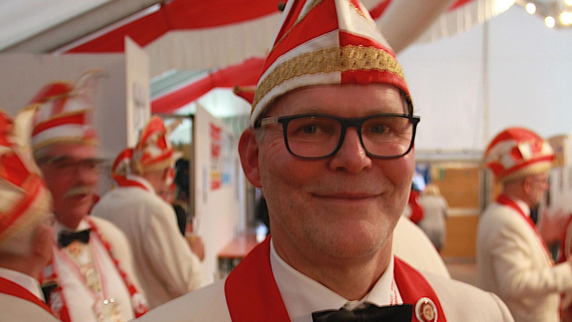 Peter Eversheim, der Vorsitzende der KG Vettweiß, trägt eine rot-weiße Narrenkappe und ein Jackett in den gleichen Farben.