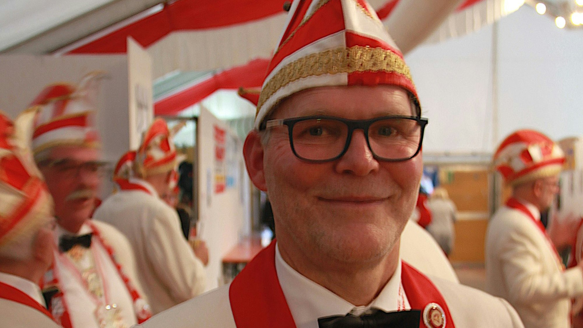 Peter Eversheim, der Vorsitzende der KG Vettweiß, trägt eine rot-weiße Narrenkappe und ein Jackett in den gleichen Farben.