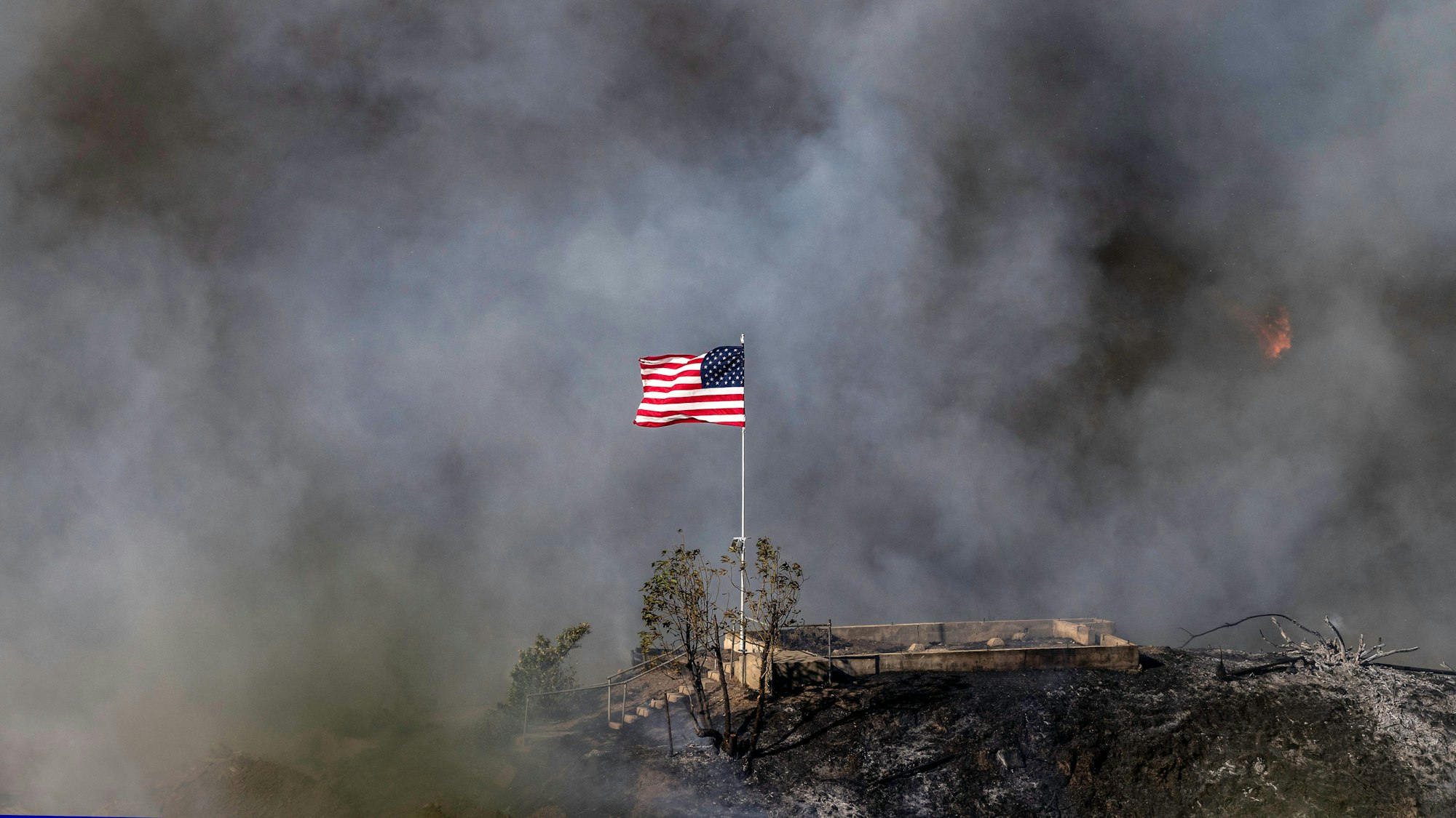 11.01.2025, USA, Los Angeles: Eine amerikanische Flagge weht über einem Teil des Mandeville Canyon, der durch das Palisades-Feuer zerstört wurde. Foto: Mark Edward Harris/ZUMA Press Wire/dpa +++ dpa-Bildfunk +++