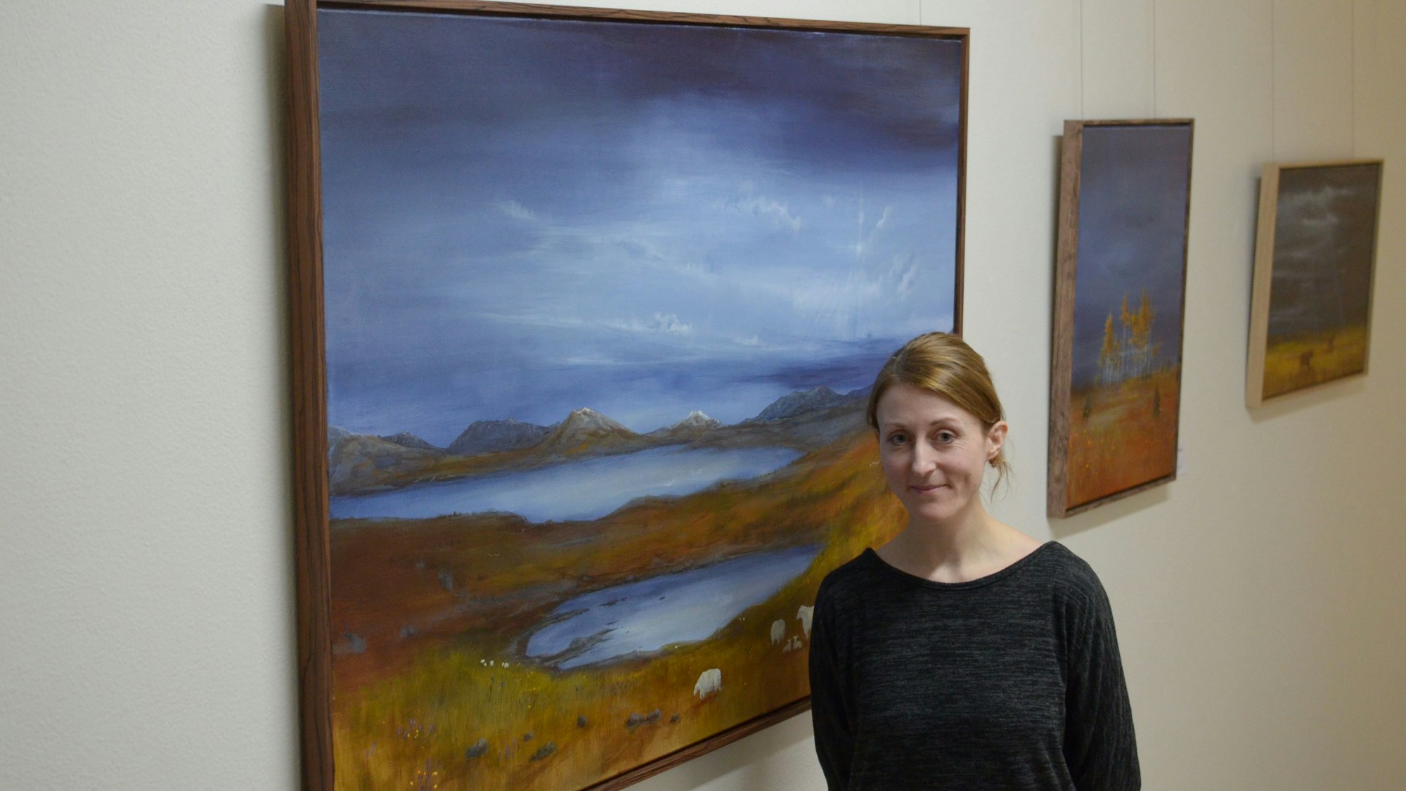 Eine Frau steht vor einem Gemälde an der Wand, im Hintergrund hängen weitere Bilder.