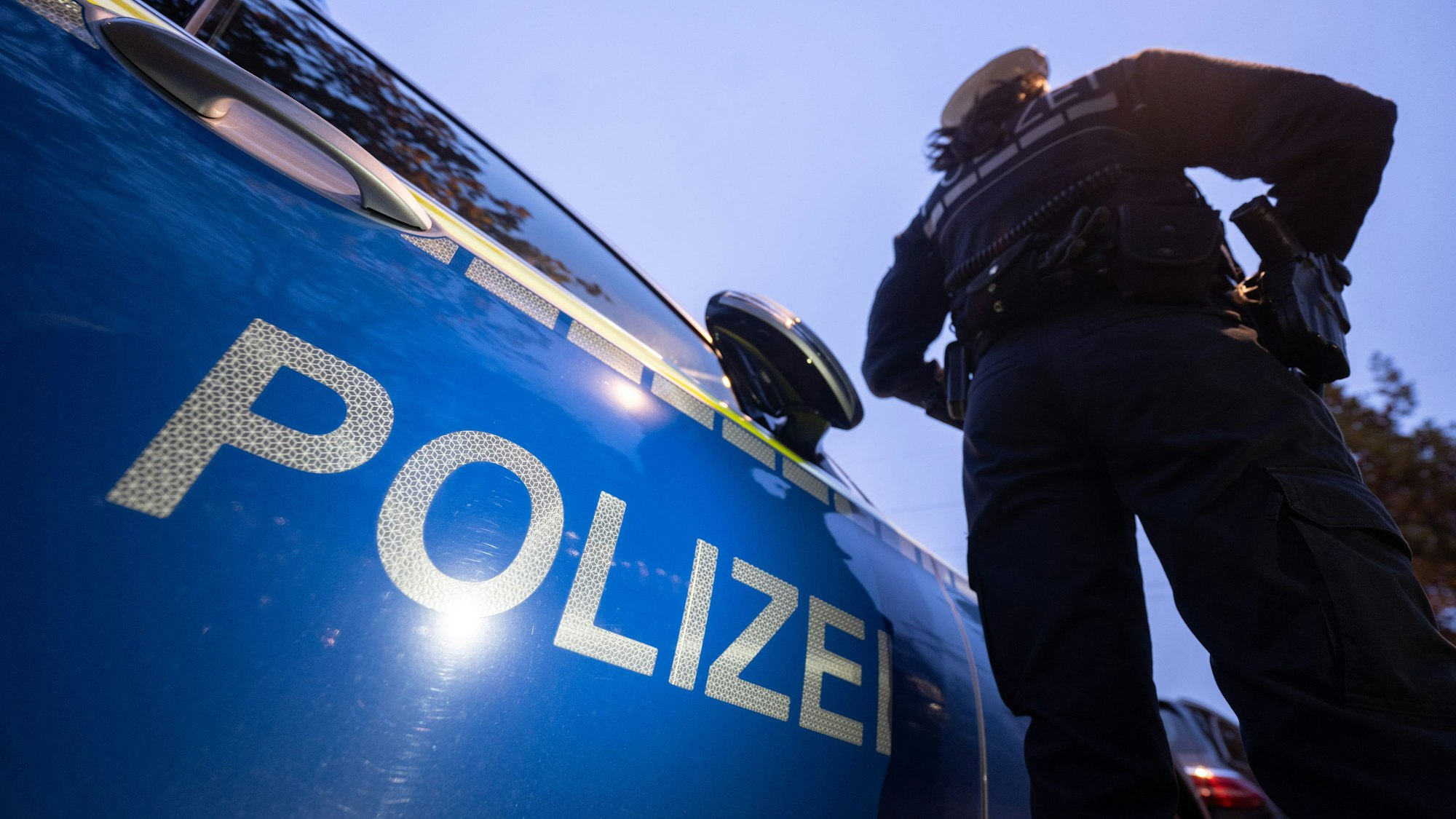 Eine Polizistin steht neben einem Polizeifahrzeug.