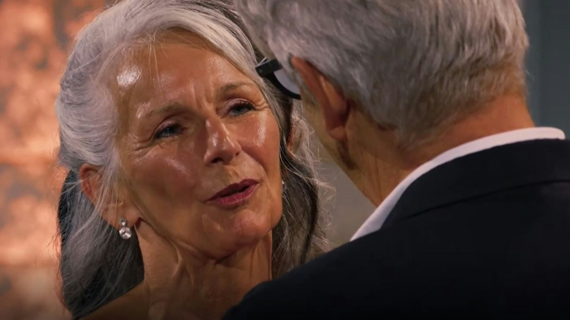 Die 62-jährige Sabine aus Troisdorf ist links im Bild zu sehen. Sie spitzt während des Sprechens die Lippen in Richtung von Franz, der rechts im Bild mit dem Rücken zum Betrachtenden steht.