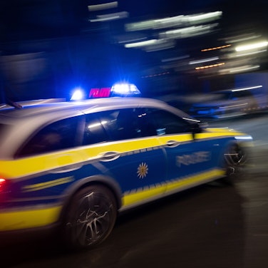 Ein Polizeifahrzeug fährt mit Blaulicht an einem Gebäude vorbei