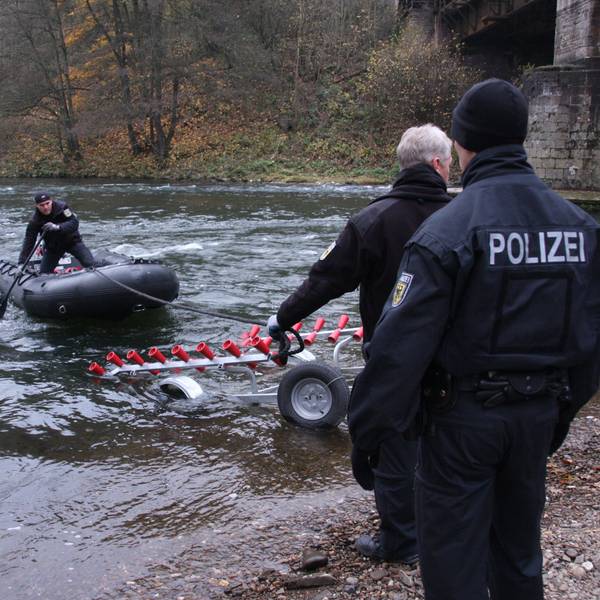 Ein Polizist steht in einem Boot, das noch auf dem Wasser schwimmt, ein Anhänger und zwei weitere Polizisten stehen bereit.