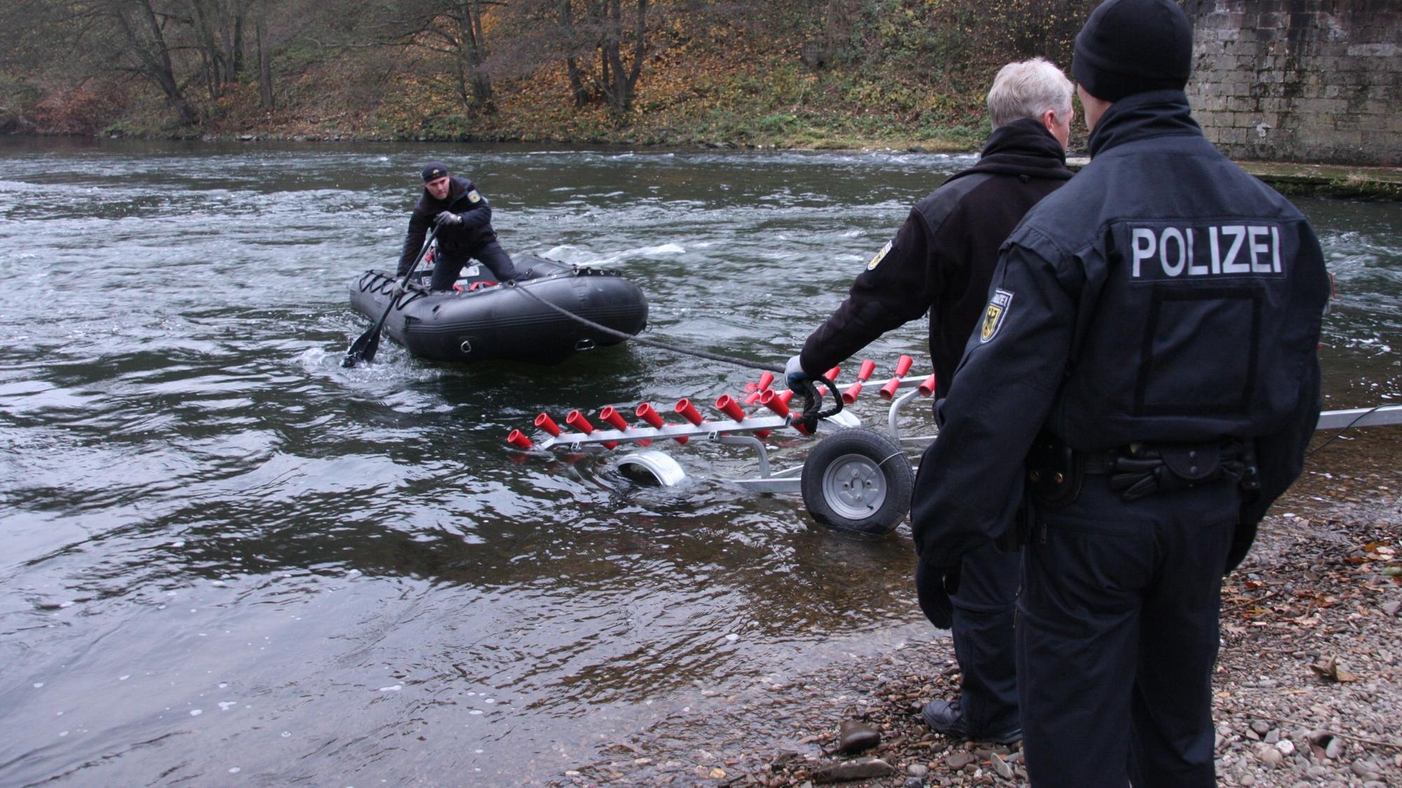 Ein Polizist steht in einem Boot, das noch auf dem Wasser schwimmt, ein Anhänger und zwei weitere Polizisten stehen bereit.