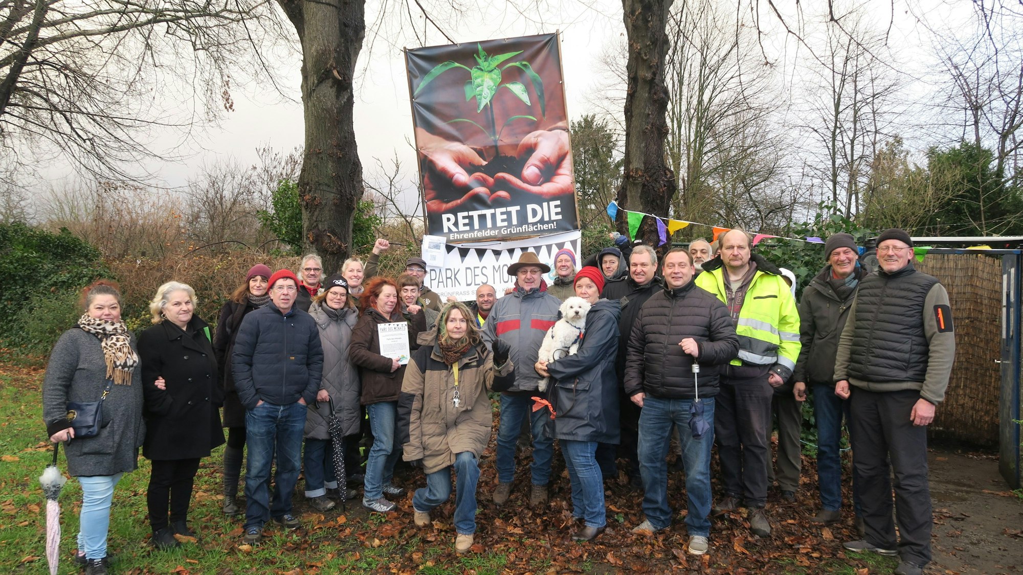 Eine Gruppe Menschen steht auf einer Wiese vor einer Grünanlage.