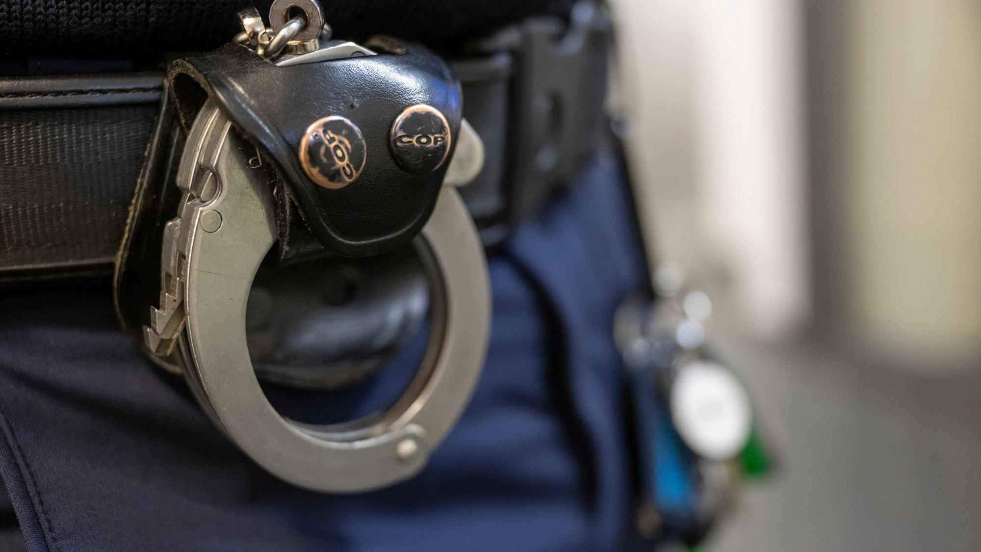 Eine Handschelle hängt am Gürtel eines Polizisten.