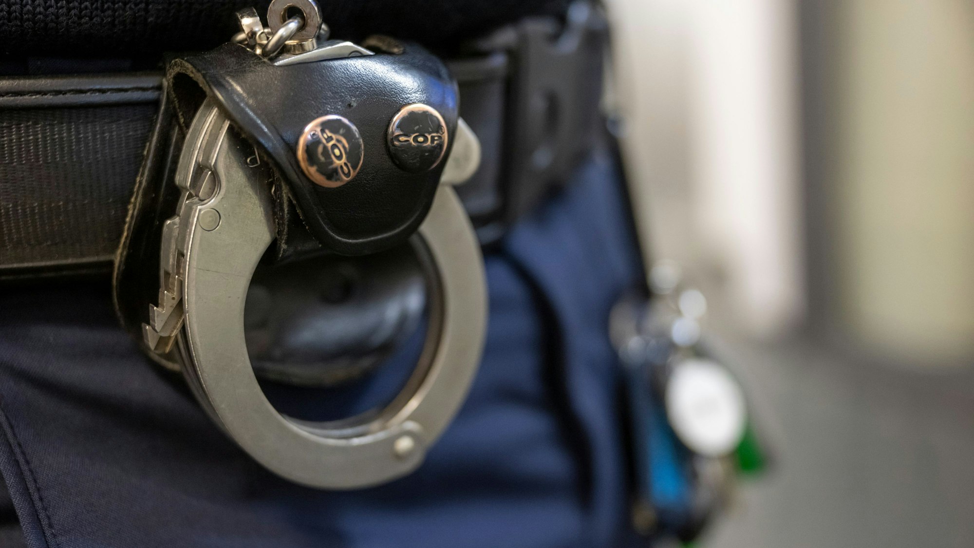 Eine Handschelle hängt am Gürtel eines Polizisten.