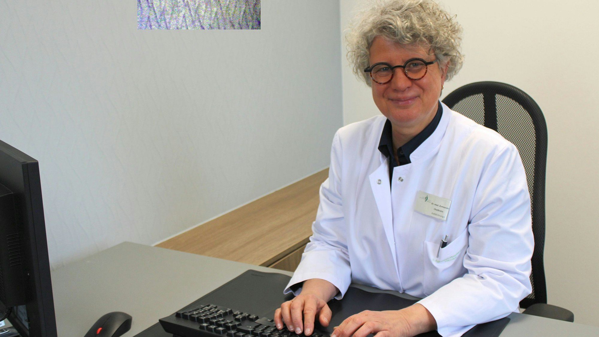 Auf dem Bild ist eine Ärztin zu sehen, die an einem Computer sitzt.