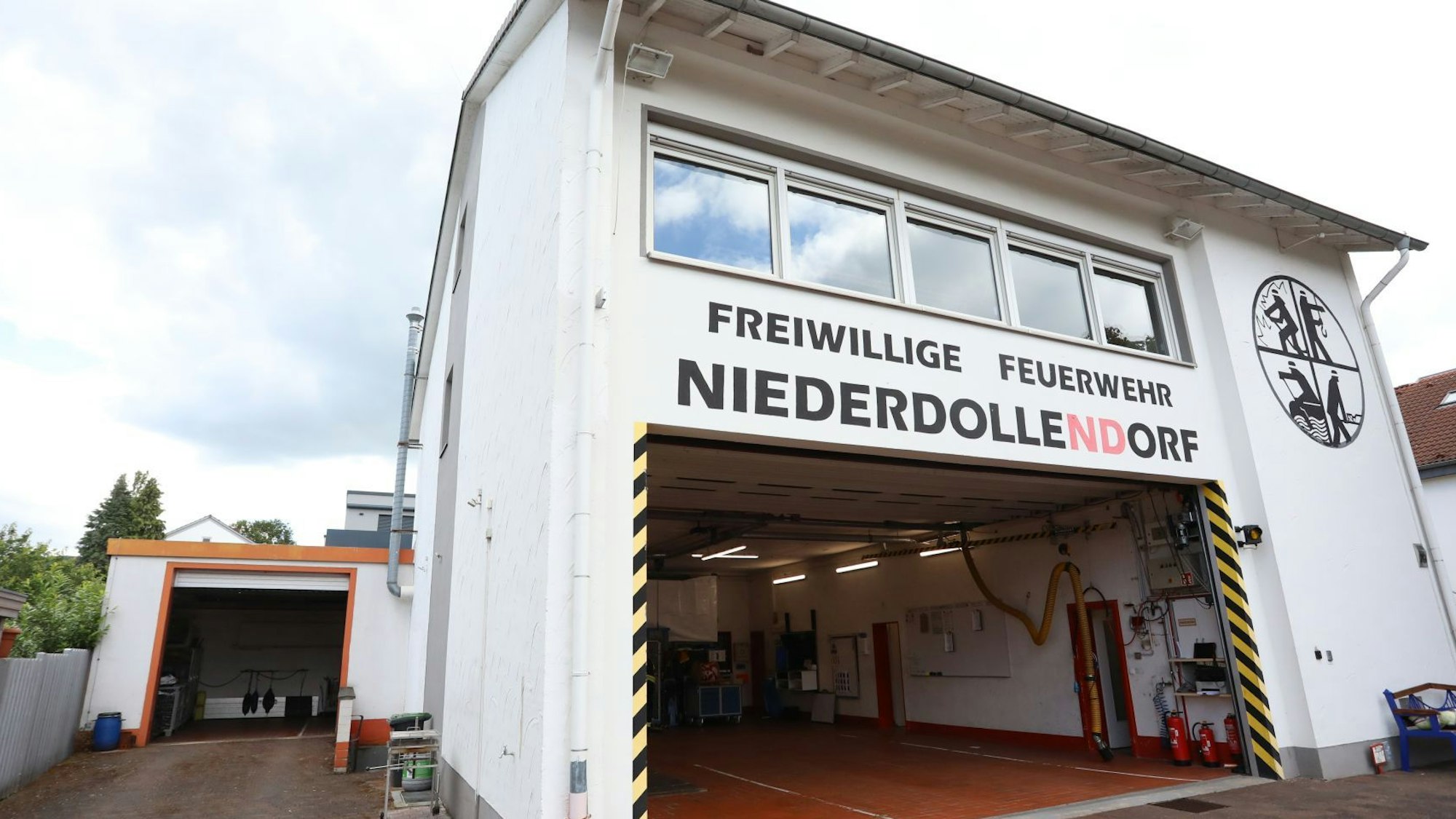 Ein Gerätehaus der Freiwilligen Feuerwehr in Niederdollendorf, an dem das Rolltor geöffnet und die Fahrzeughalle leer ist.