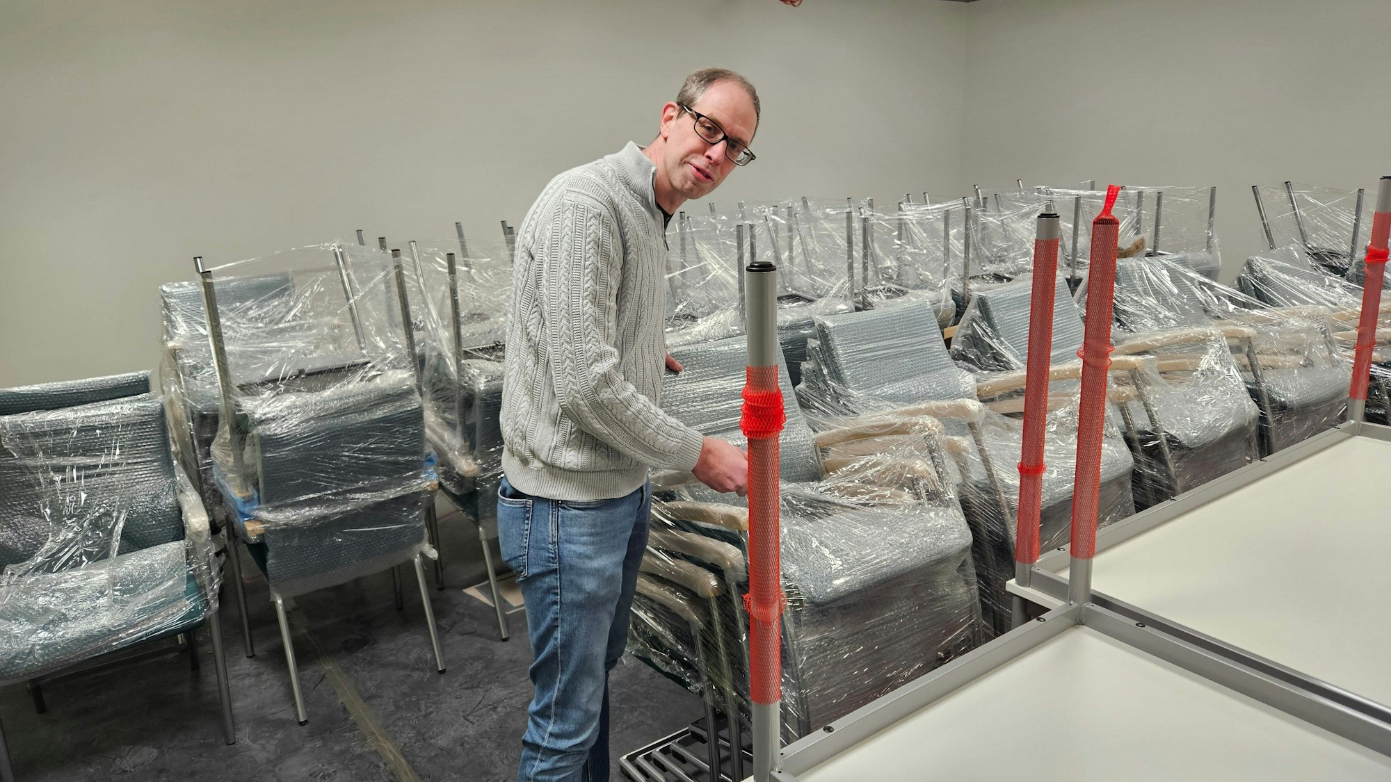 Stefan Marenbach steht vor einer großen Zahl noch eingepackter Stühle.