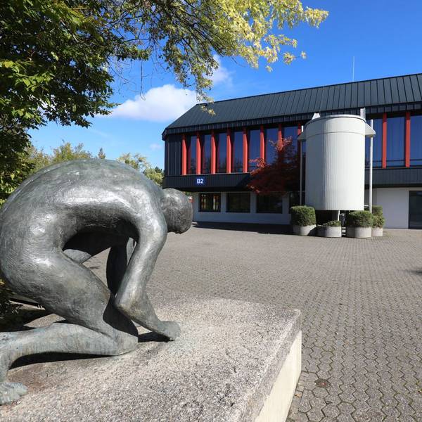 Eine Bronzestatue vor einem Trakt des Schulzentrums Oberpleis.