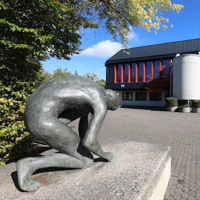 Eine Bronzestatue vor einem Trakt des Schulzentrums Oberpleis.