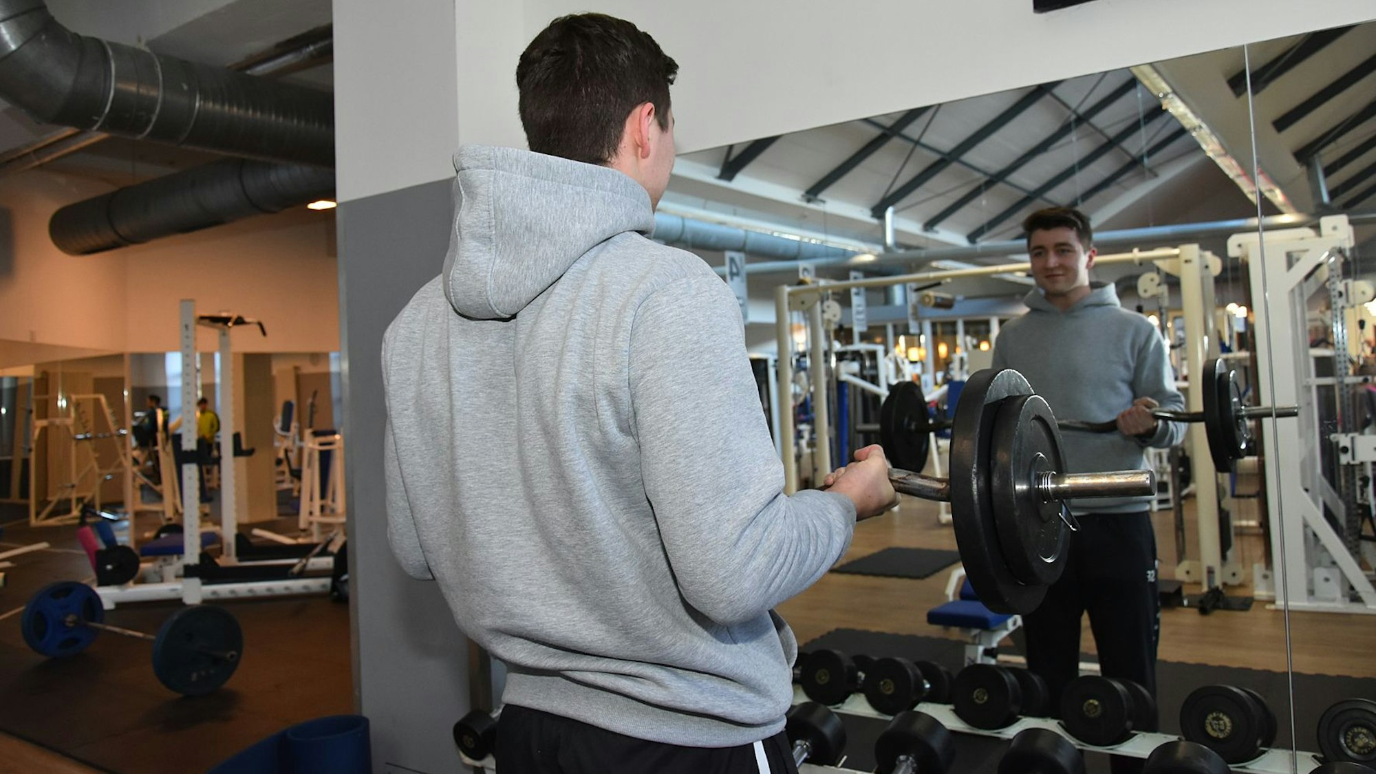 Ein junger Mann stemmt vor einem Spiegel eine Hantel.