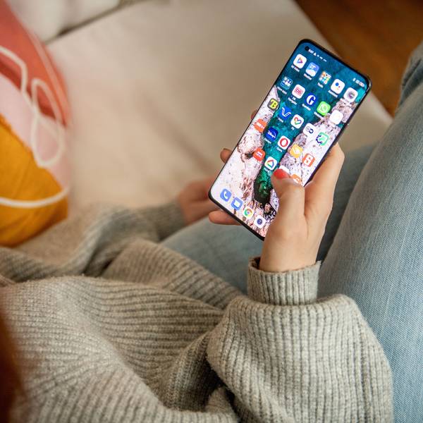 Eine Frau sitzt auf dem Sofa und schaut auf ihr Smartphone.