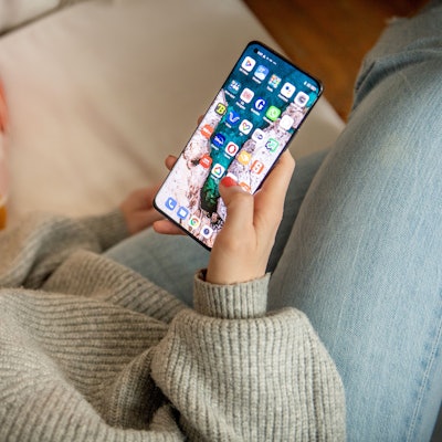 Eine Frau sitzt auf dem Sofa und schaut auf ihr Smartphone.