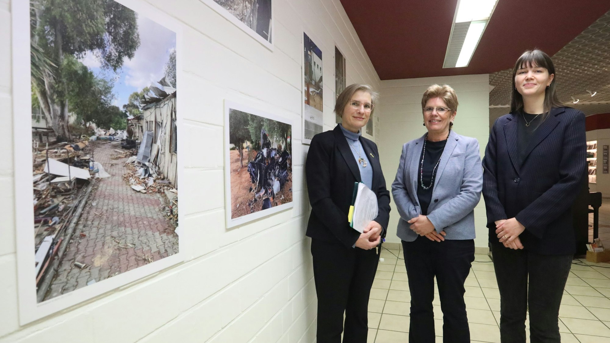 Drei Frauen neben einer Wand mit großformatigen Fotos.