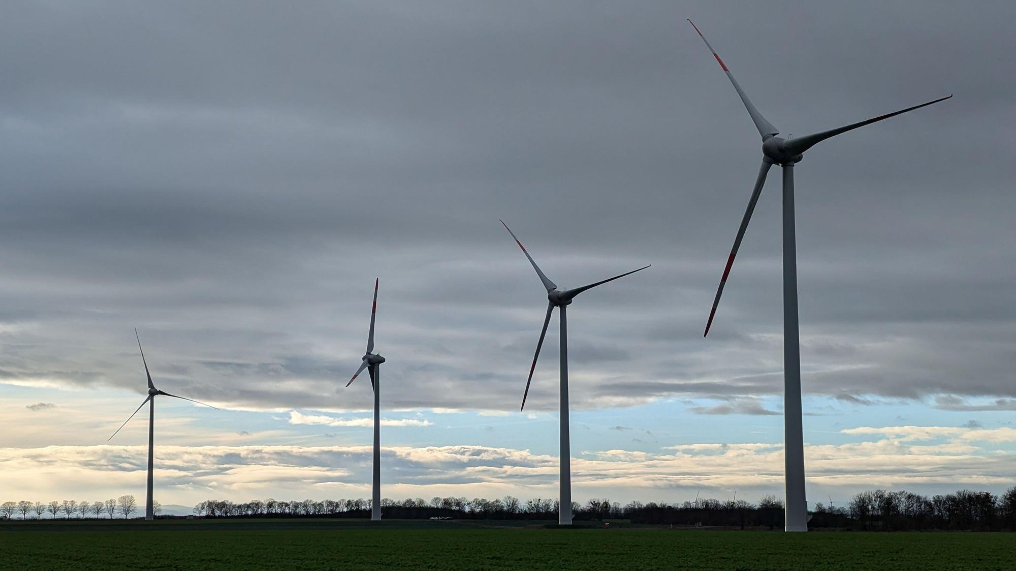 Windkraftanlagen sind vor einem bewölkten Himmel in Hürth zu sehen.
