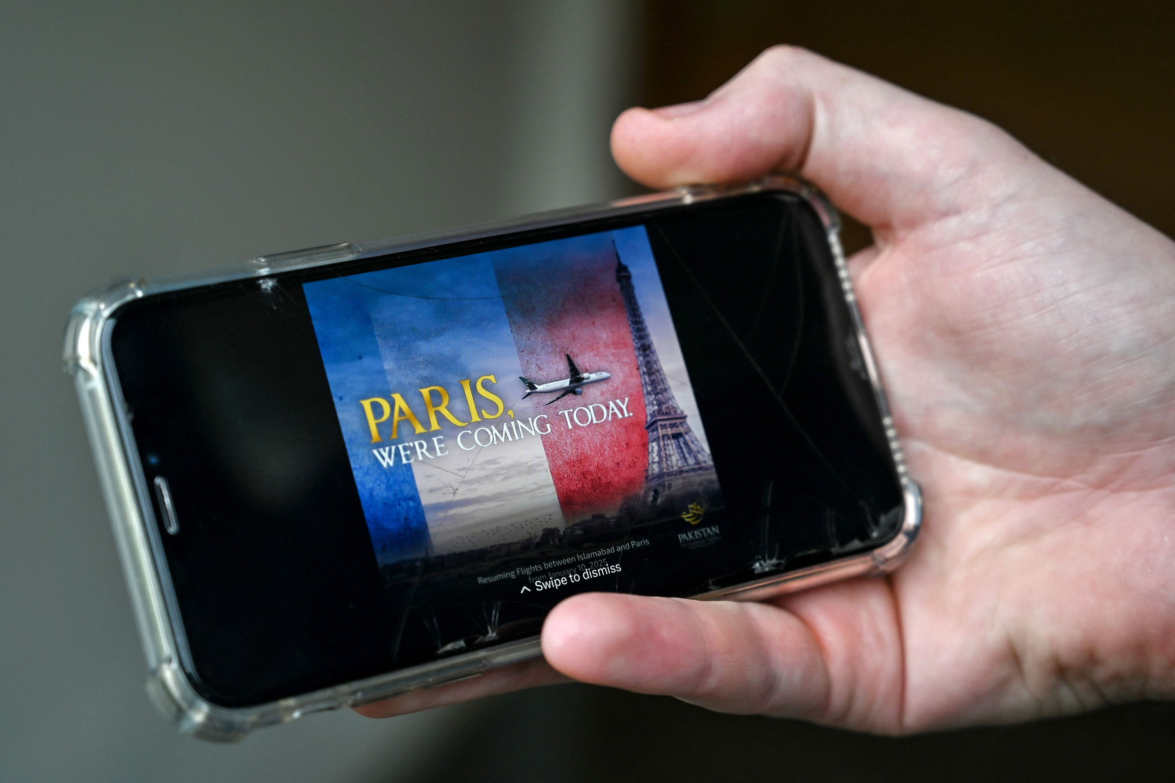 Ein Mann schaut sich auf seinem Mobiltelefon in Islamabad eine Werbung des Flugzeugs der Pakistan International Airlines (PIA) an, das auf den Eiffelturm zufliegt.