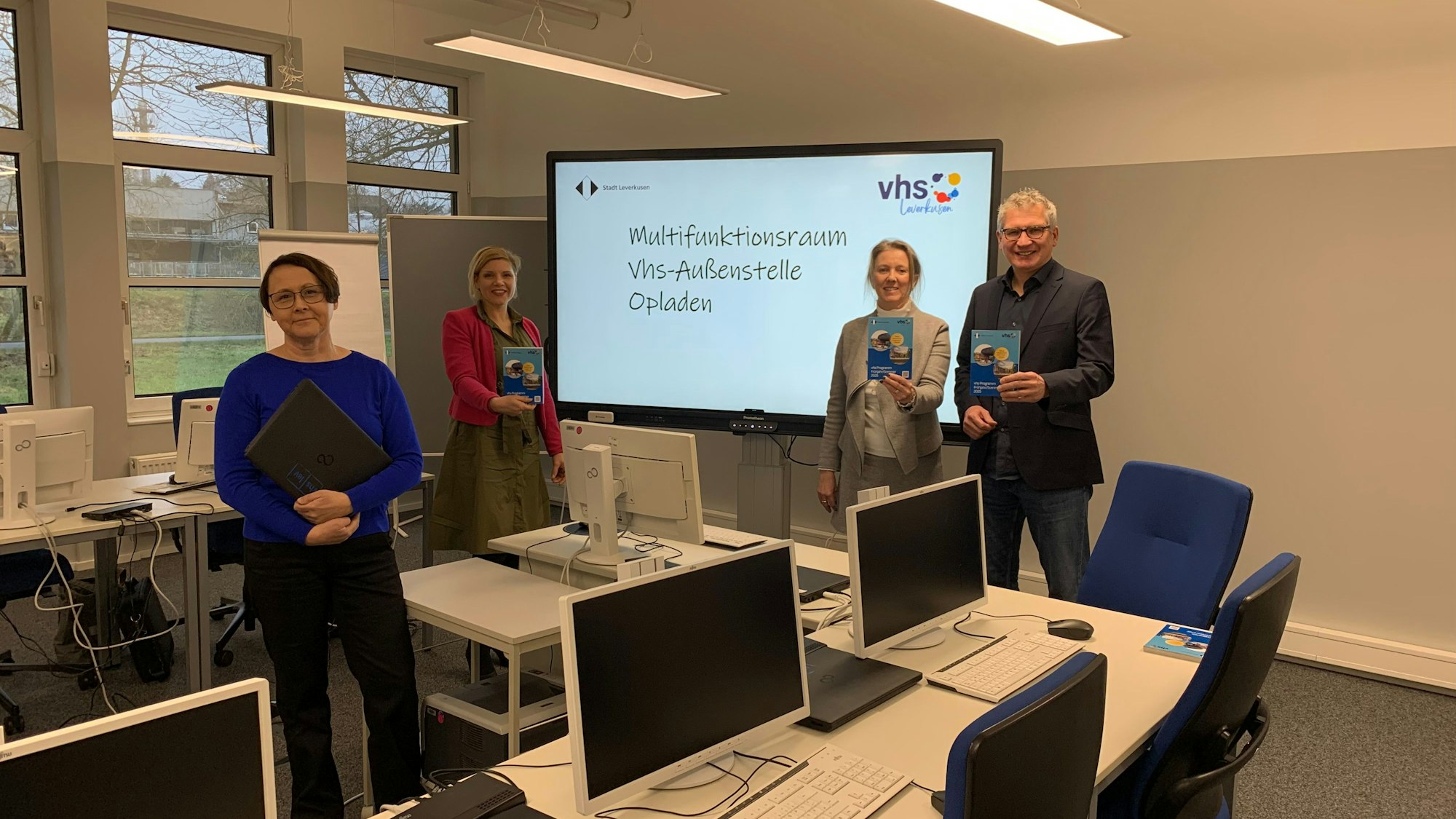 Drei Frauen und ein Mann stehen vor einem Smartboard und zwischen Computern.