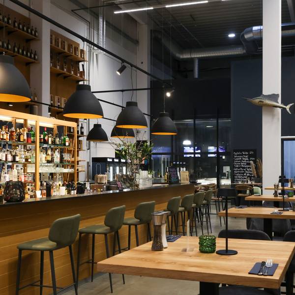 Die Bar mit großen Lampenschirmen darüber ist zu sehen, ebenso einige Hochtische mit Stühlen in dem noch nicht geöffneten Lokal.