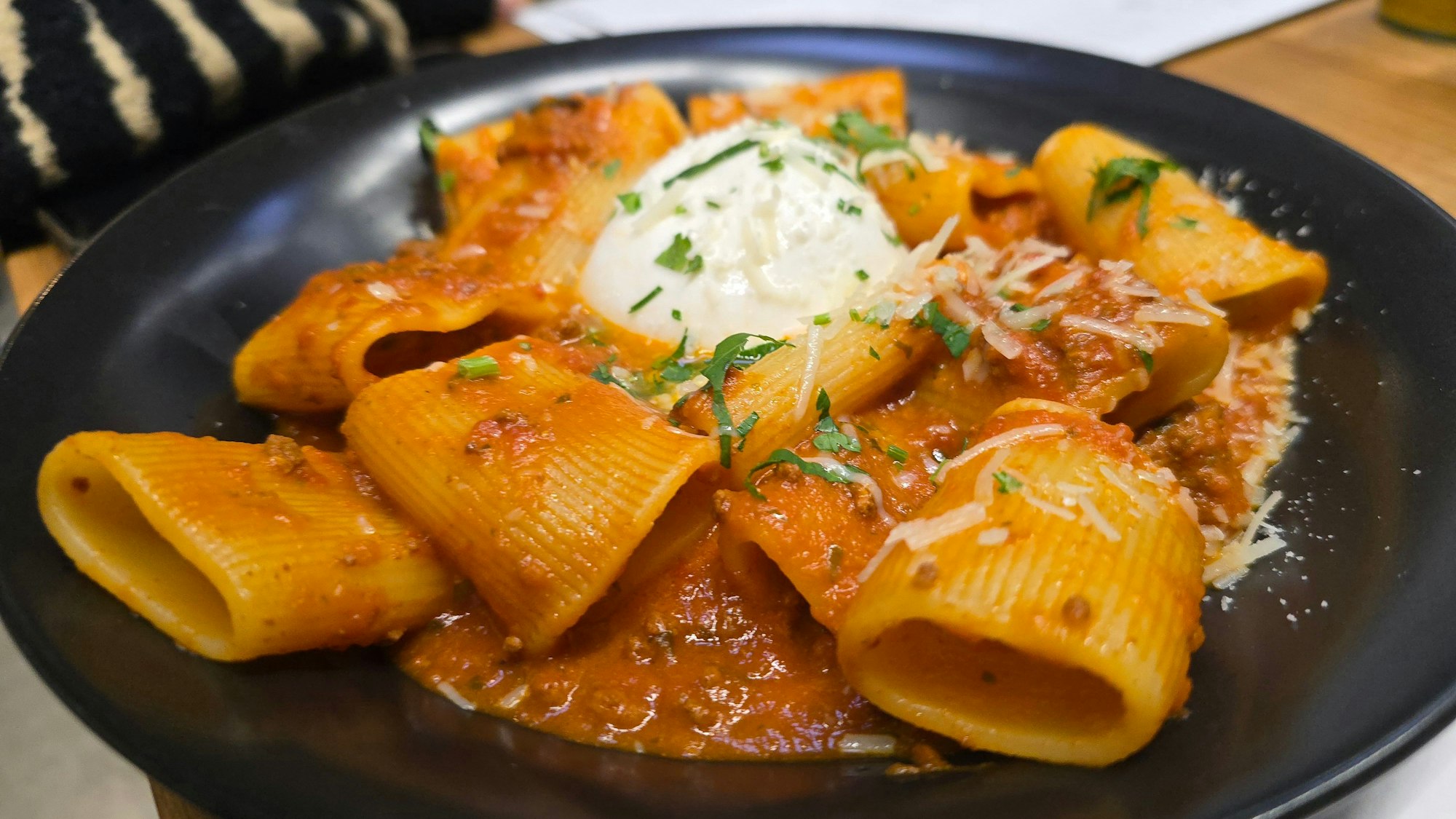 Ein Tellergericht mit Röhrennudeln und Sauce ist zu sehen. In der Mitte die weiße Burrata.