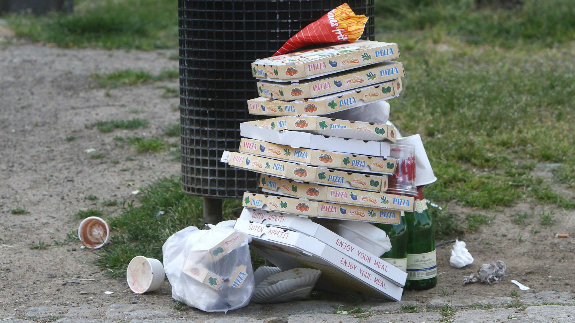 Pizzakartons stapeln sich neben geleerten Sektflaschen vor einem überfüllten Mülleimer in der Altstadt von Köln.