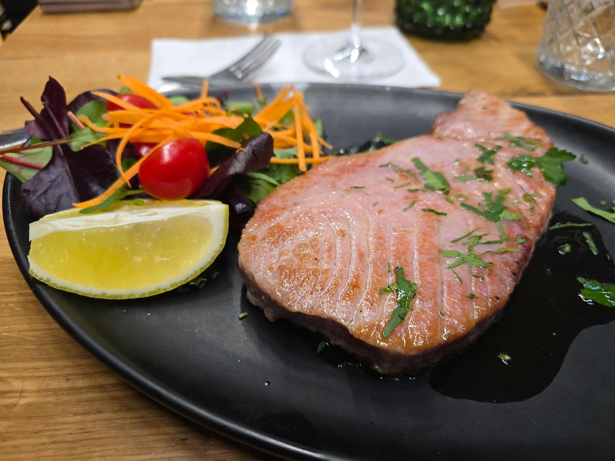 Das Steak liegt auf einem schwarzen Teller neben Salatgarnitur und einem Zitronenschnitz.