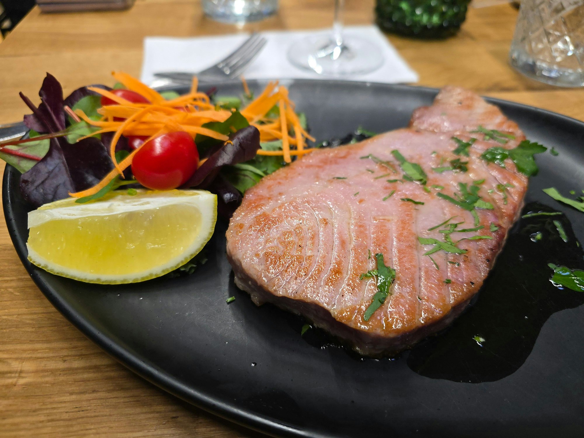 Das Steak liegt auf einem schwarzen Teller neben Salatgarnitur und einem Zitronenschnitz.