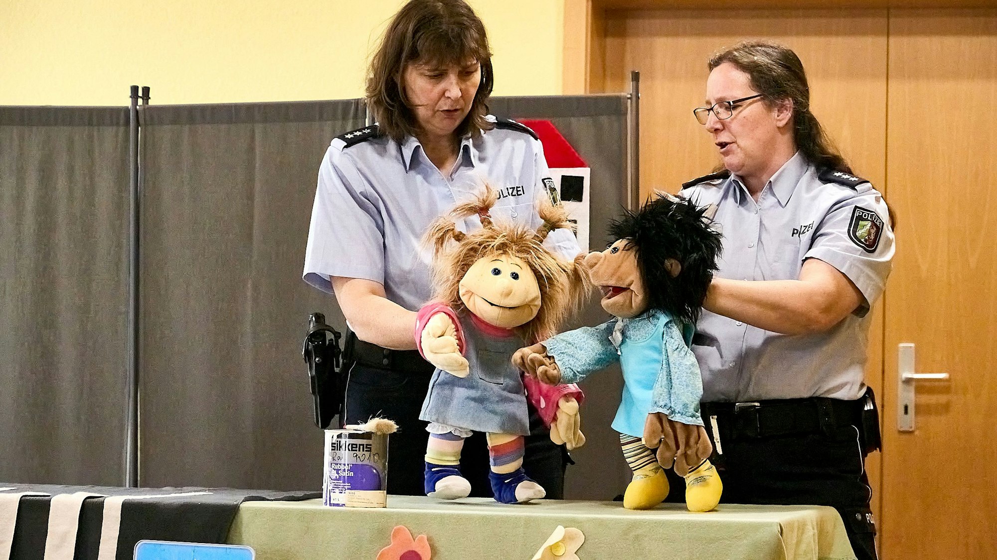 Zwei Polizistinnen in Uniform halten Handpuppen, die auf einem Tisch stehen. Sie sind Teil eines Theaterstücks, das die Polizei in einem Präventionsprogramm in Kindergärten einsetzt.