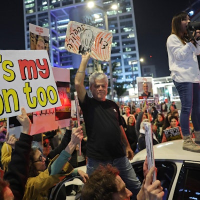 Menschen mit Plakaten; eine Demonstrantin auf einem Autodach mit Megafon.