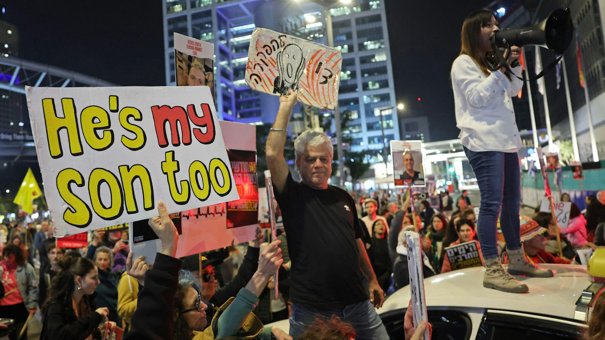 Menschen mit Plakaten; eine Demonstrantin auf einem Autodach mit Megafon.