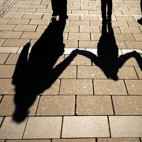 Die Schatten von zwei Erwachsenen und einem Kind fallen in den Morgenstunden auf den Asphalt.