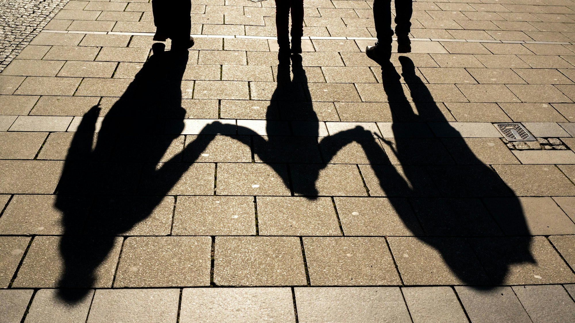 Die Schatten von zwei Erwachsenen und einem Kind fallen in den Morgenstunden auf den Asphalt.