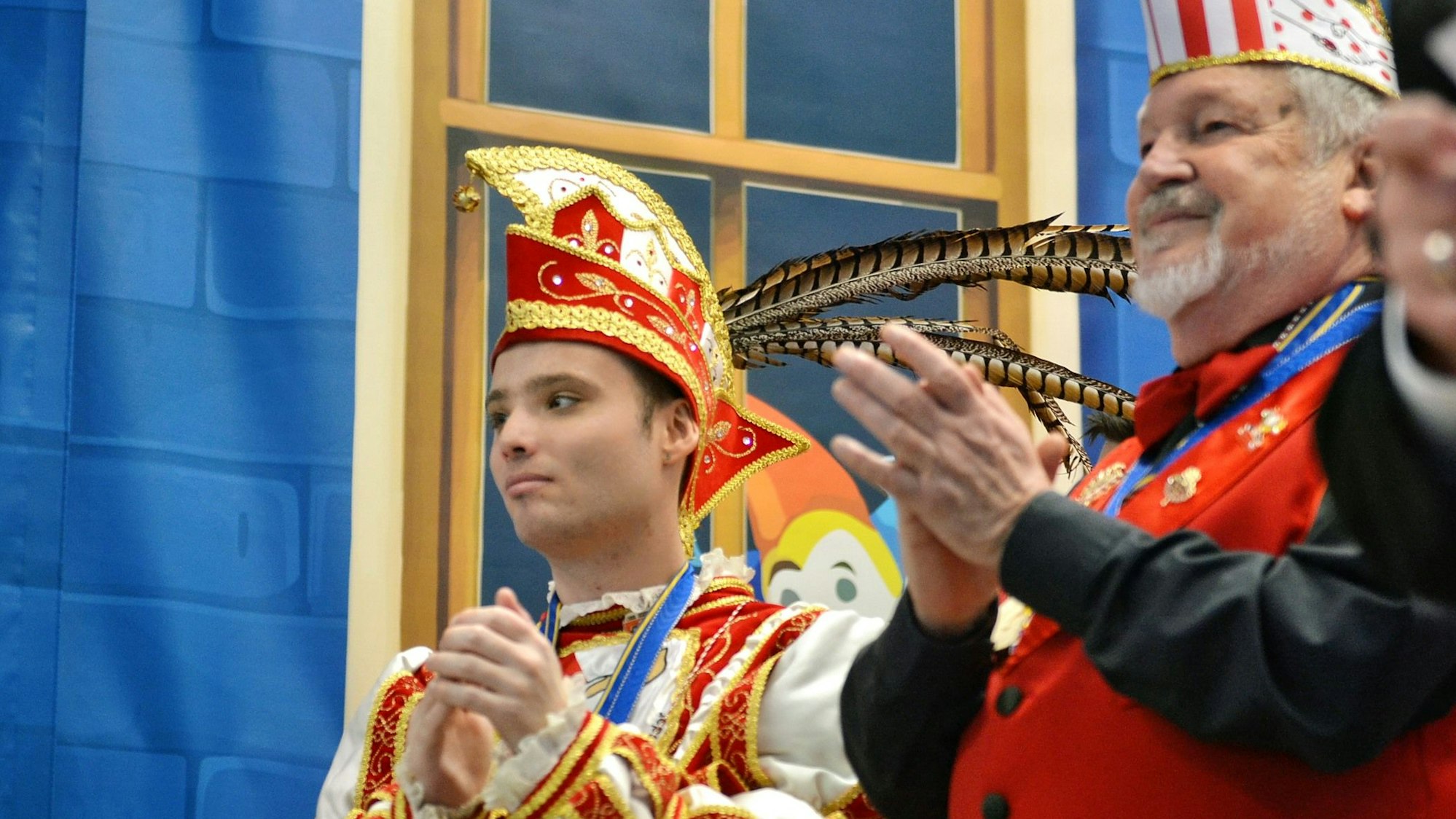 Der junge Prinz applaudiert auf der Bühne zusammen mit einem anderen Karnevalisten nach einer Darbietung.
