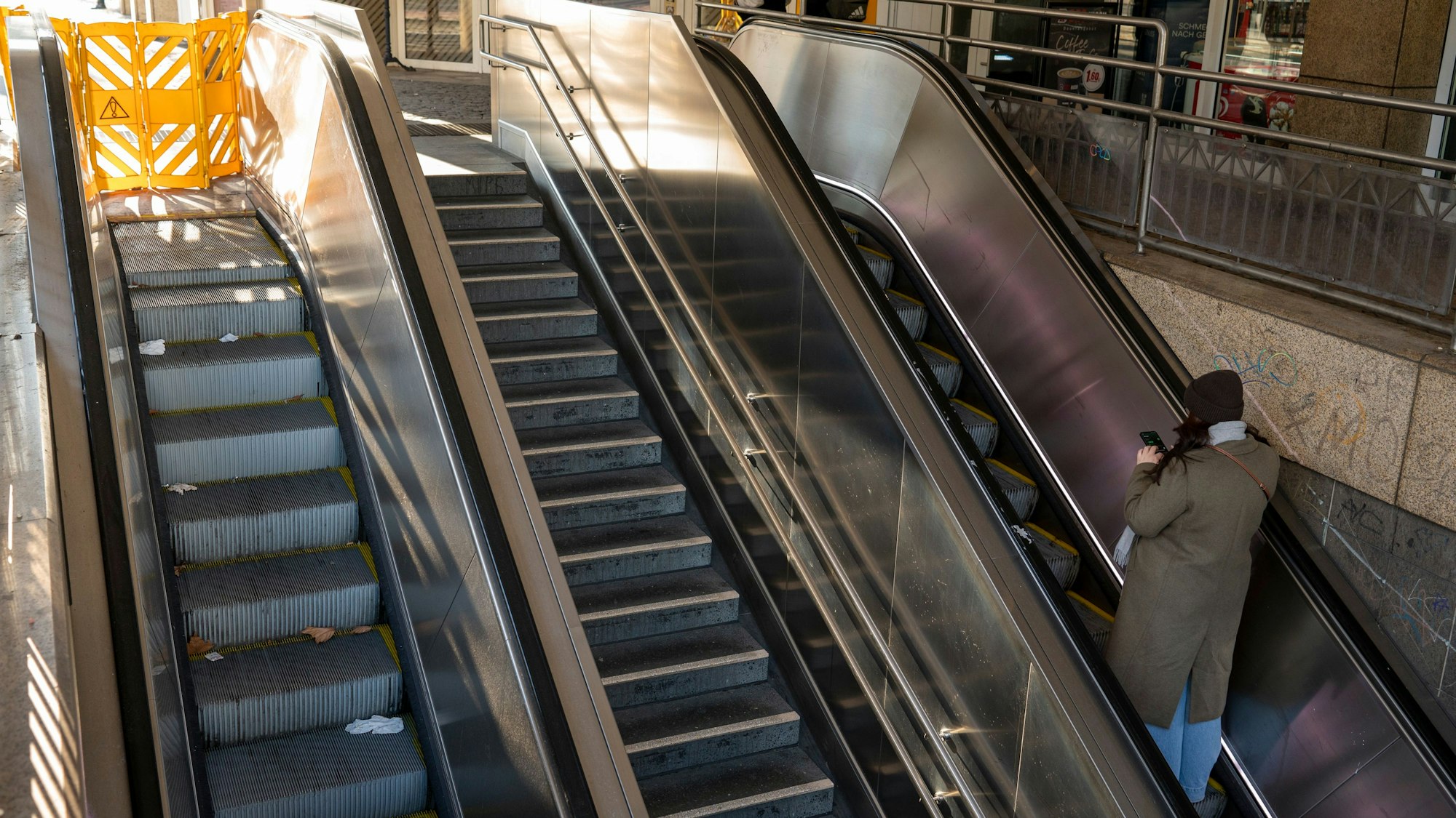 Zu sehen sind zwei Rolltreppen und eine Steintreppe am Friesenplatz. Eine Rolltreppe ist mit einem gelben Zaun abgesperrt.