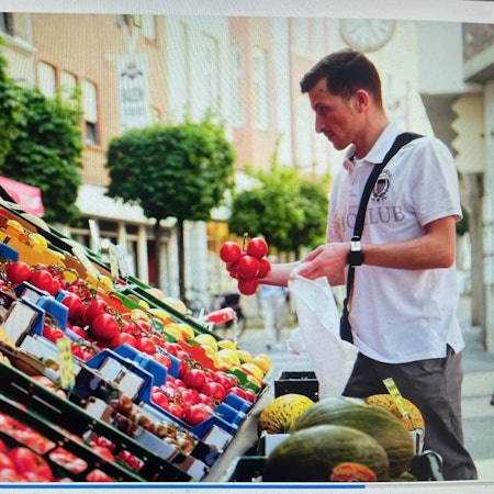 Das Bild zeigt eine Szene aus dem Imagefilm. Ein Mann sucht am Freiluftstand eines Supermarkts Gemüse aus.