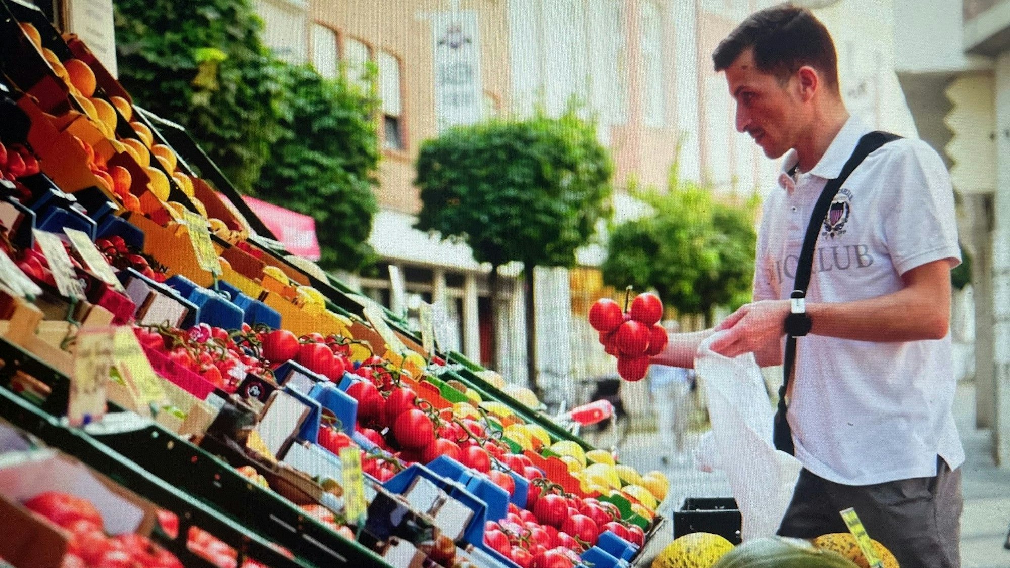 Das Bild zeigt eine Szene aus dem Imagefilm. Ein Mann sucht am Freiluftstand eines Supermarkts Gemüse aus.