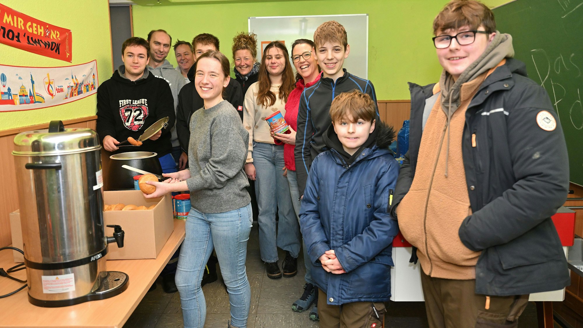 Messdienerinnen und Messdiener stehen um einen Topf mit Würstchen, eine Messdienerin schneidet ein Brötchen auf.