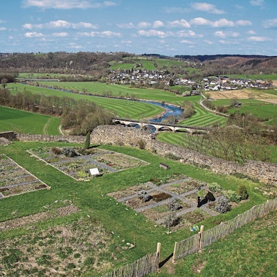 Blick über Gartenbeete mit Bruchsteinmauer in ein Tal.