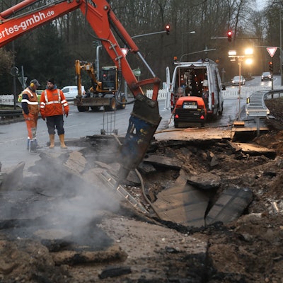 Ein kleiner Bagger und Arbeiter stehen an der abgesackten Stelle der Fahrbahn der Friedrich-Eber-Straße.