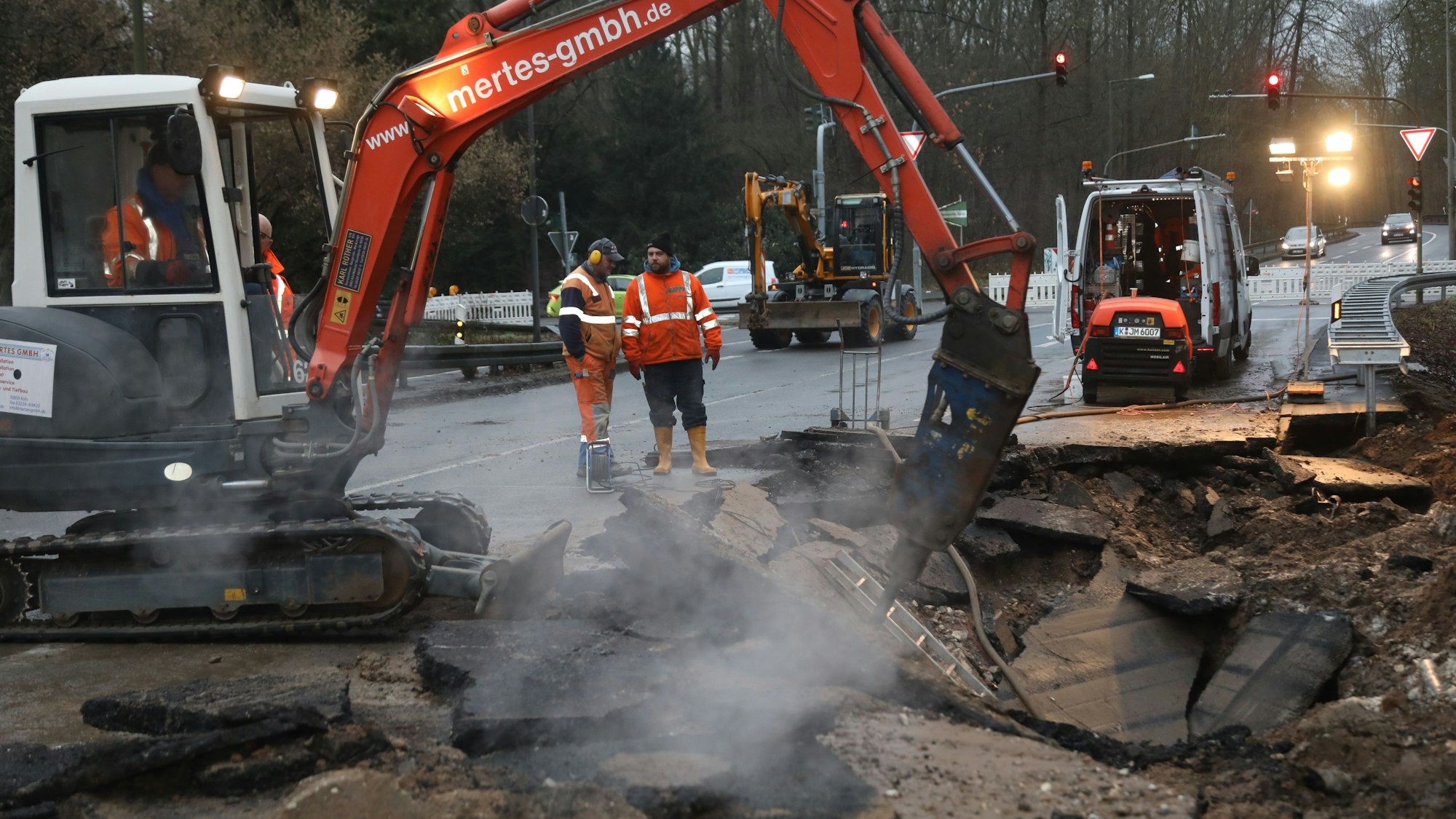 Ein kleiner Bagger und Arbeiter stehen an der abgesackten Stelle der Fahrbahn der Friedrich-Eber-Straße.