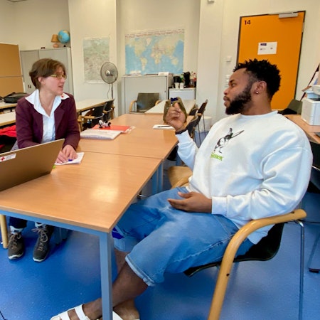 Ein Mann und eine Frau sitzen sich in der Flüchtlingsunterkunft Weilerswist an einem Tisch gegenüber und unterhalten sich.