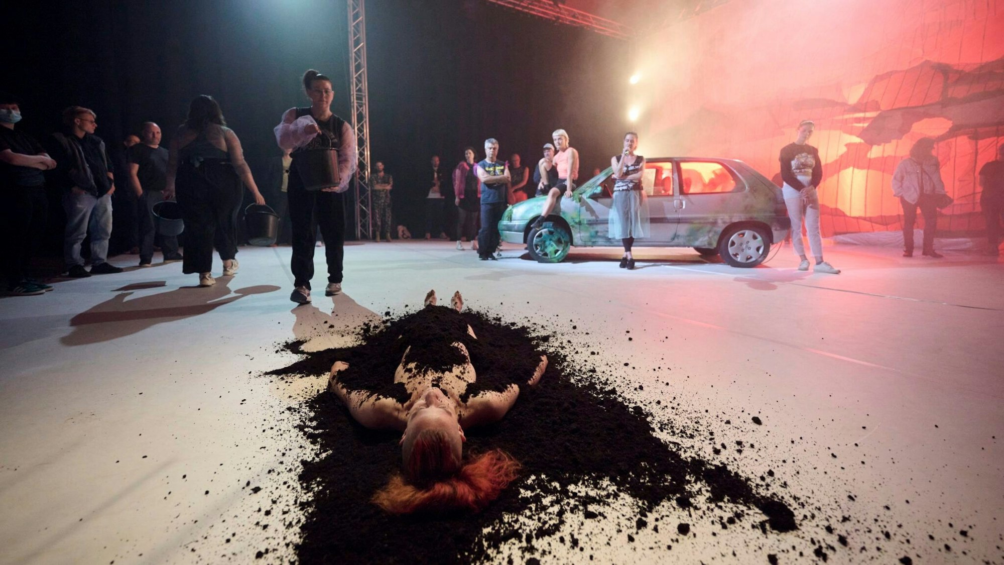 Eine mit Erde begrabene Person liegt nackt auf dem Boden